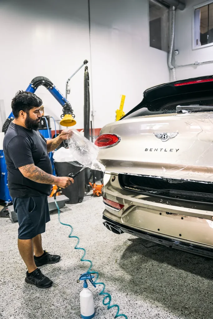 Technician masking a Bentley for refinishing at Enthusiast Auto Works